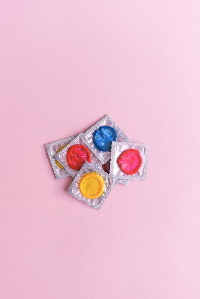 A vibrant collection of multicolored condoms arranged on a pink background, symbolizing safe sex and sexual health awareness.